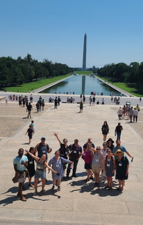 A group of teachers pose happily at the foot of the stairs at the Lincoln Memorial. The reflecting pool and Washington Monument are in the background.