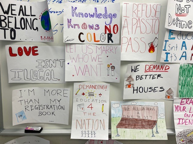 Close-up view of student-made protest signs. One says "Knowledge Knows No Color."