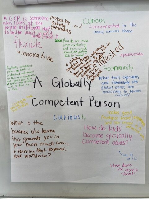 A large sheet of paper with ideas and questions written by teachers, centered on the phrase "A Globally Competent Person." (1 of 3)