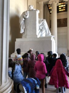 A group of children in winter coats listen to a Park Ranger at the foot of the Lincoln Statue in the Lincoln Memorial.