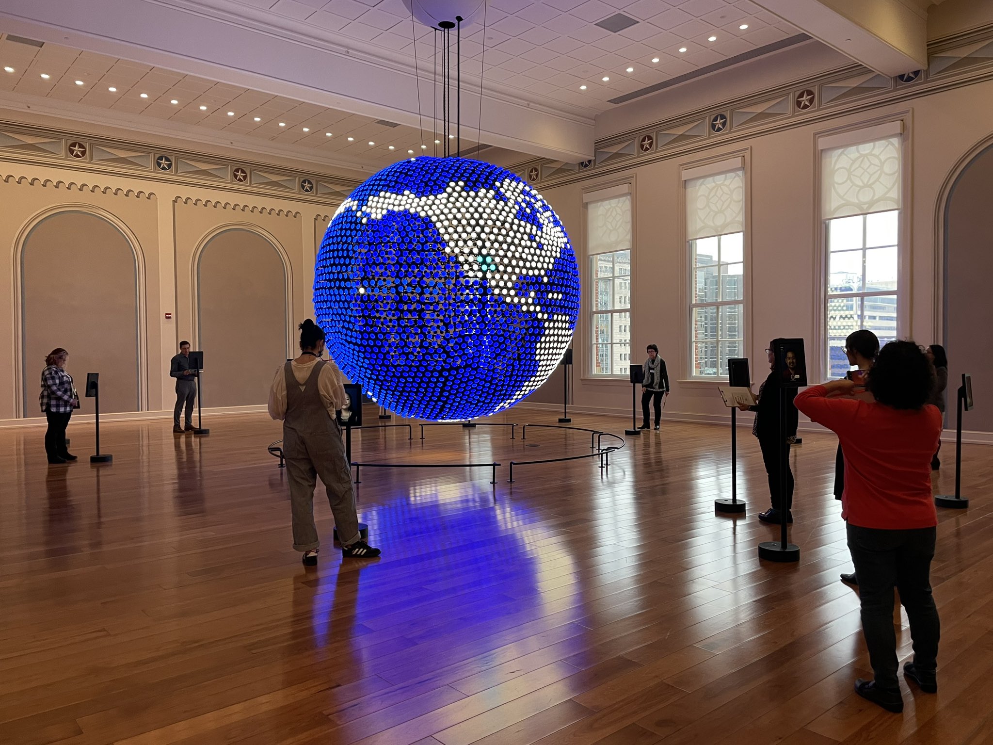 Teachers and visitors inside the Planet Word Museum World Languages gallery. A bright, glowing, blue globe hangs from the center of the ceiling.