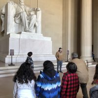 A group of three students stand in front of the Lincoln statue in the Lincoln Memorial